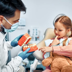 Children dentist in San Bernardino showing a young girl a tooth model during a pediatric dental visit in the dental chair